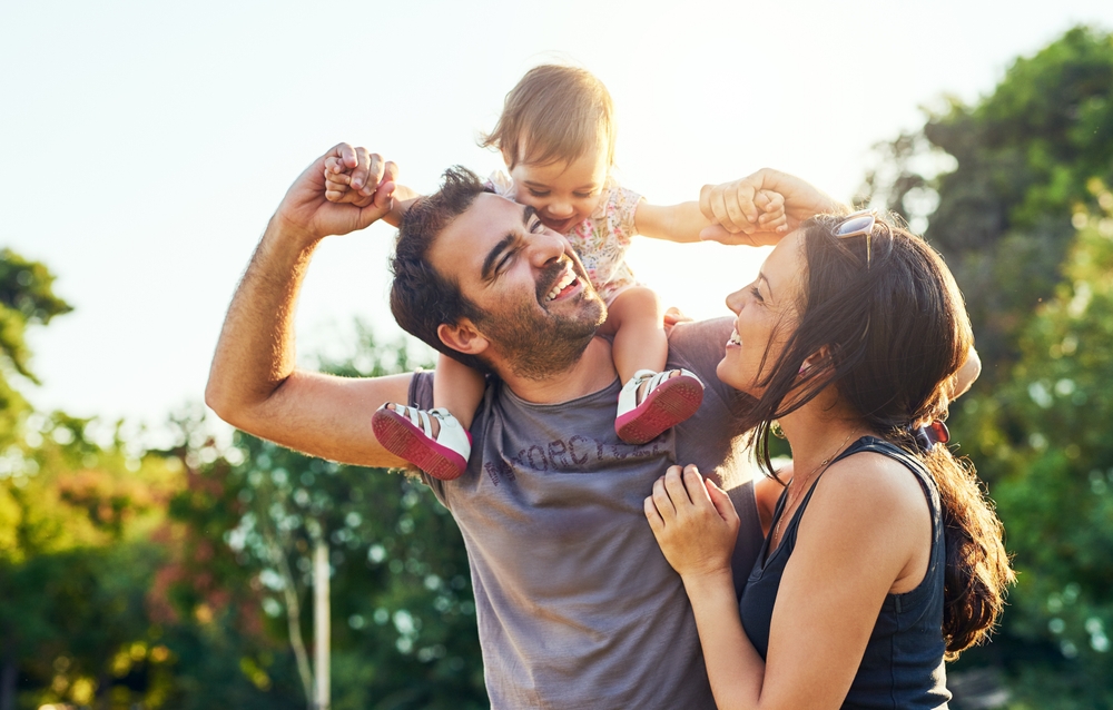 Family,,Dad,And,Daughter,On,Shoulders,In,Park,With,Mom,